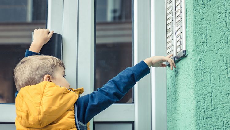 Kind steht am Klingelbrett eines Wohnblocks